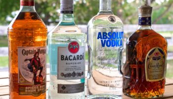 Четыре бутылки алкоголя: Captain Morgan, Bacardi, Absolut Vodka и Crown Royal, стоящие на деревянной поверхности.